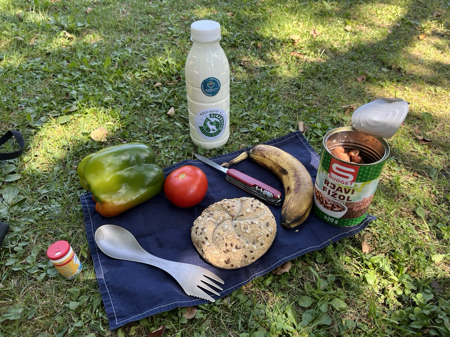 Lunch on the ground, bread roll, banana, canned beans, tomato, pepper, kefir