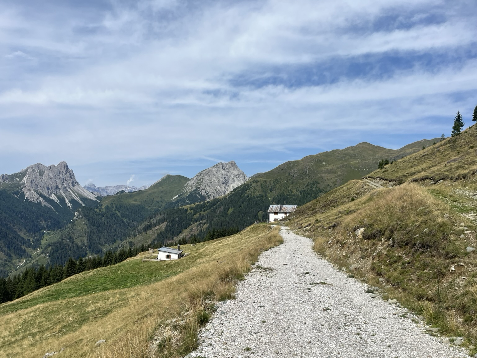 Gravel road on a mountain side, views to tall rocky mountains, the Dolomites in the distance